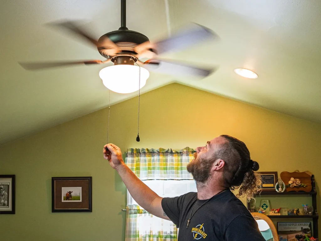 A PowerHaus employee pulling on the cord of a ceiling fan in a home